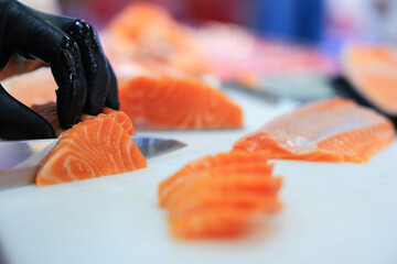 The chef is preparing, handling, deboning or slicing fresh salmon. Close up hand of chef with salmon sashimi.