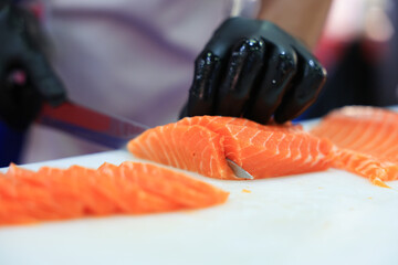 The chef is preparing, handling, deboning or slicing fresh salmon. Close up hand of chef with salmon sashimi.