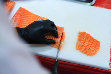 The chef is preparing, handling, deboning or slicing fresh salmon. Close up hand of chef with salmon sashimi.