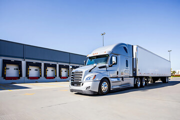 Modern Silver Semi Truck Ready for Delivery Parked at Loading Dock with Bright Blue Sky Ready to Ship Goods Across the Country