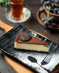 Delicious chocolate cheesecake served on a black plate with a fork shadow and grapes in the background