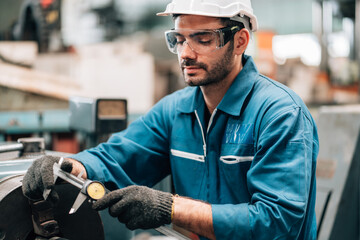 A factory worker, dressed in a blue jumpsuit, white hard hat, and safety glasses, is meticulously...