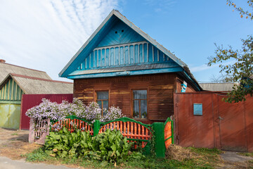 Fototapeta premium A narrow street in a village with small wooden houses and flower beds against a blue sky.