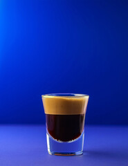 Close-up of a fine espresso shot in clear glass on blue background. Concept for modern healthy beverages, homebrew drinks and healthy drinks.