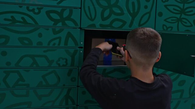 Person retrieving package from modern parcel locker system with decorative green facade and floral pattern design. Concept of automated delivery services, urban logistics and contactless pickup.