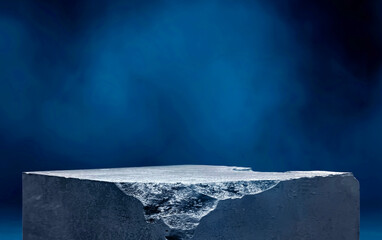 Abstract image of a weathered concrete block or podium with a jagged, cracked top and textured sides, set against a blue background with a fog or smoke effect. product displayed podium.
