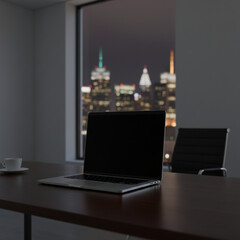 Laptop on a desk in a dark office with city skyline at night
