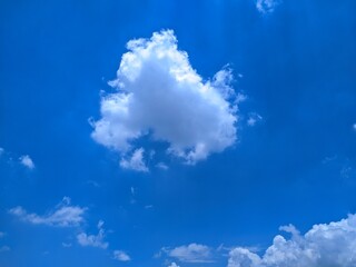 A puffy cumulus cloud drifts across a  blue sky. Fluffy, white clouds dot the bottom of the frame, hinting at a beautiful, sunny day.
