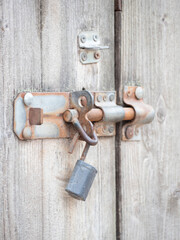 Close-up of a heavy, iron bolt and padlock securing a wooden door. The weathered texture of the wood and the corroded metal speak of age, history, and security.