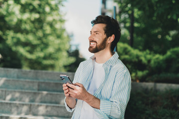 Obraz premium Young man outdoors holding smartphone with a cheerful expression enjoying leisure time in a serene city environment