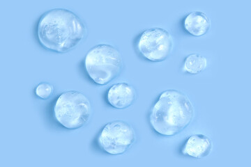 Moisturizing serum or essence: thick gel drops with bubbles on clean blue background.