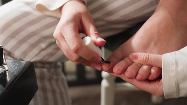 Medium view girl seated on chair painting toe nail with black polish, hand steady, foot supported, casual home grooming, self care routine, close detail of precise brush strokes on toenails