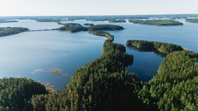 Explore the stunning views along the Punkaharju esker road in Finland. Lush forests embrace the winding path, offering breathtaking glimpses of tranquil waters and picturesque islands on a clear day.