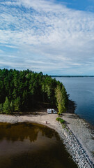 Relaxing camping scene at Lake Saimaa showcases a tranquil shoreline surrounded by lush greenery. A camper van awaits visitors to explore the serene waters and natural beauty of Finland.