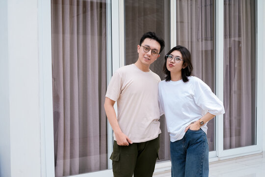 A relaxed couple stands close smiling, with arms around each other outside a modern glass window - Powered by Adobe