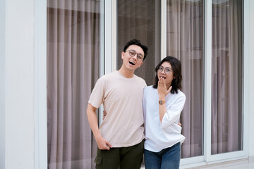 A relaxed couple stands close smiling, with arms around each other outside a modern glass window