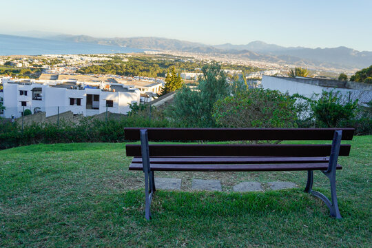 A park bench overlooking the cityscape of Cabo Negro, Morocco, with mountains in the background. A quiet travel scene