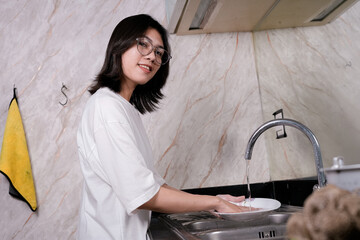 A young woman in a white tee washes dishes at a sleek kitchen sink