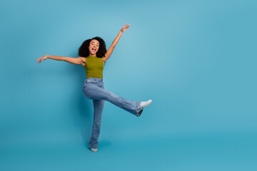 Fototapeta premium Joyful young woman in casual outfit dancing playfully on blue background, expressing happiness and energy