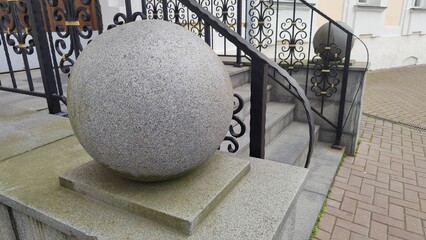 Large gray granite sphere on a pedestal in front of building with black wrought iron fence and...