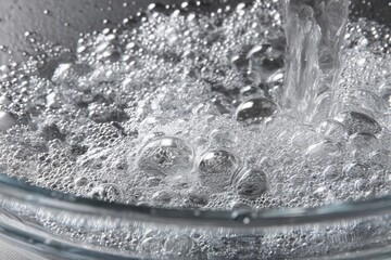 Close-up of soap bubbles forming under a stream of water in a clean transparent dish