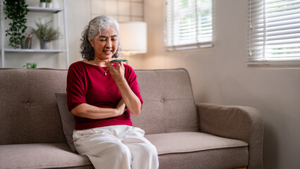 Older Asian woman actively uses smartphone voice message feature at home connecting digitally with family friends