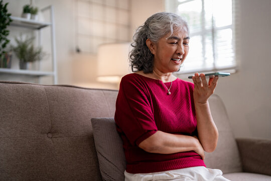 Older Asian woman communication phone call home senior using smartphone speakerphone conversation comfortable living room staying connected family