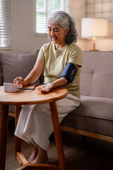 Asian older woman measures blood pressure at home monitoring health independently in her comfortable living room self care for senior wellness