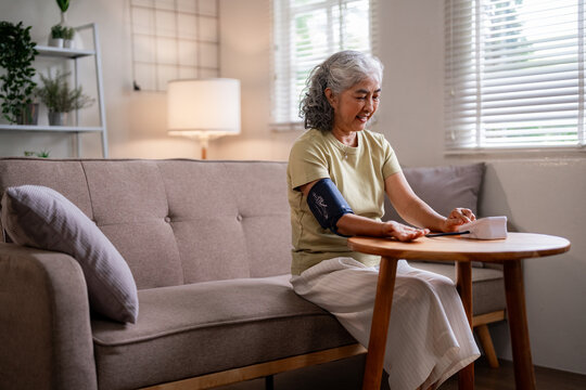 Asian older woman independently monitors blood pressure at home for proactive health management and personal wellness - Powered by Adobe