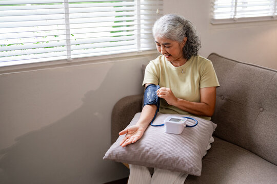 Older Asian woman independently monitors blood pressure at home for personal health management wellness self care prevention healthy living routine
