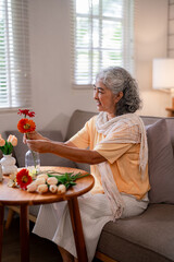 Asian older woman happy arranging fresh flowers home living room senior female enjoying tranquil...
