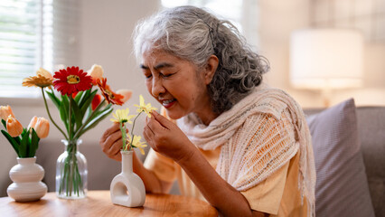 Asian senior woman joyful home living room fragrant yellow flowers peaceful moment cozy indoor happiness older lady wellbeing serene elder life
