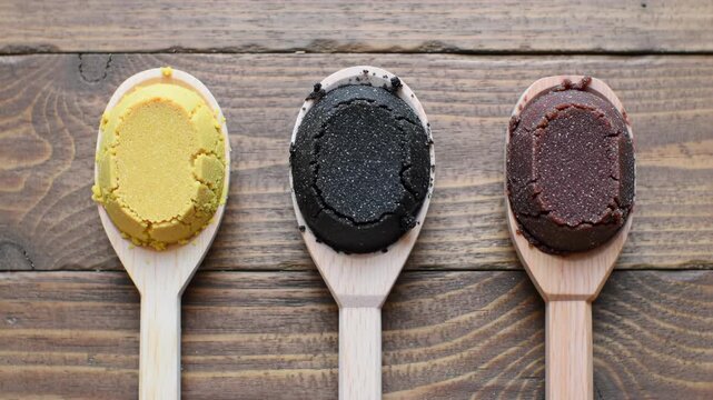Colored doughs on wooden spoons against a wooden backdrop.