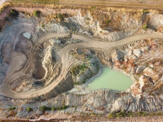 Unique aerial view of a winding dirt path through a mining area with small green water pools in the...