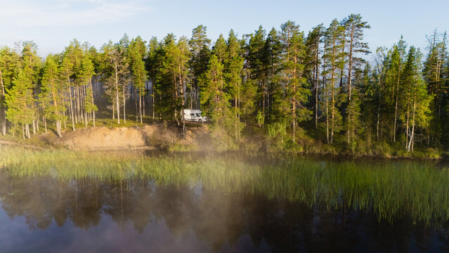 Majestic trees frame the serene waters of Hossa National Park. A camper welcomes adventurers to experience Finland natural beauty and tranquility. - Powered by Adobe