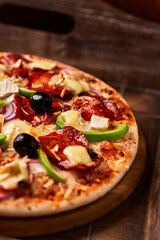 Pizza with chorizo ​​sausage, mozzarella cheese, green pepper and black olives. Rustic wooden background. Soft focus.	