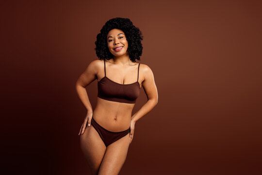 Confident woman in stylish lingerie posing against brown background, showcasing body positivity and natural beauty - Powered by Adobe