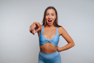 Fototapeta premium Woman in light blue activewear celebrates with excitement in a studio setting while pointing towards the camera