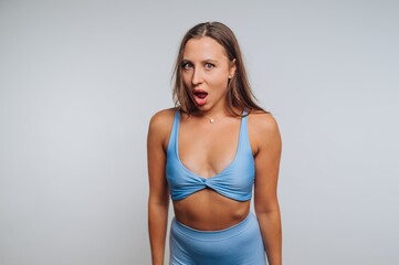 Fototapeta premium Young woman expressing surprise in stylish blue activewear during a studio photoshoot in a minimalistic setting