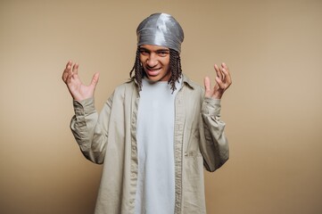 Young man expressing excitement while wearing a light-colored outfit and a headscarf in a neutral backdrop