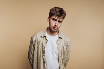 Young man poses with a serious expression against a plain background while dressed casually