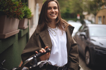 Portrait of a pretty young woman on bicycle in the city street, city transportation. Outdoor fashion portrait of elegant brunette long hair lady riding her hipster retro bike in stylish trench coat.