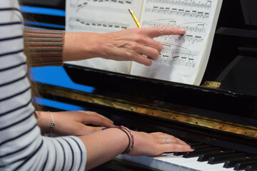 Human hands of a piano teacher explaining to a student playing the keys notes and chords on a classic black piano during a pianolesson