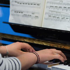 Human hands playing the keys notes and chords on a classic black piano during a pianolesson