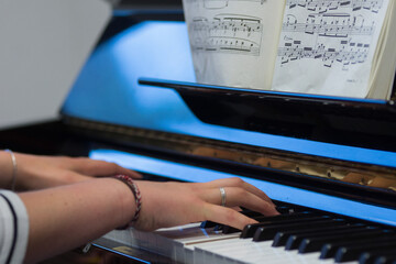 Human hands playing the keys notes and chords on a classic black piano during a pianolesson