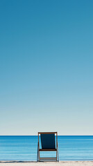 A single deck chair faces a calm blue sea under a clear sky on a quiet beach, evoking solitude and relaxation.