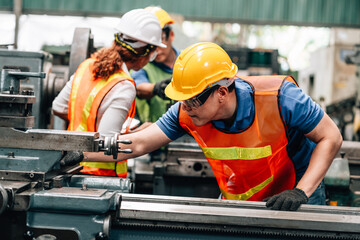 Three factory workers are actively in large industrial machines. In the foreground, a male worker...