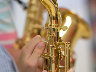 Human hand holding playing a saxophone close up with another saxophone in the background during musiclessons