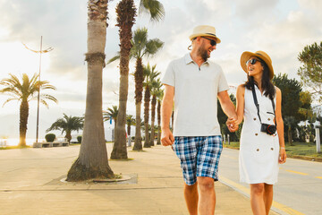 Young couple tourists walking hand in hand along Batumi promenade with palm trees and seaside view on sunrise, concept of tourism, vacation, lifestyle and romantic travel in Georgia