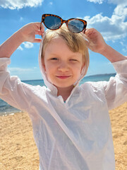 A happy girl in a white shirt and sunglasses on sandy beach on a sunny summer day